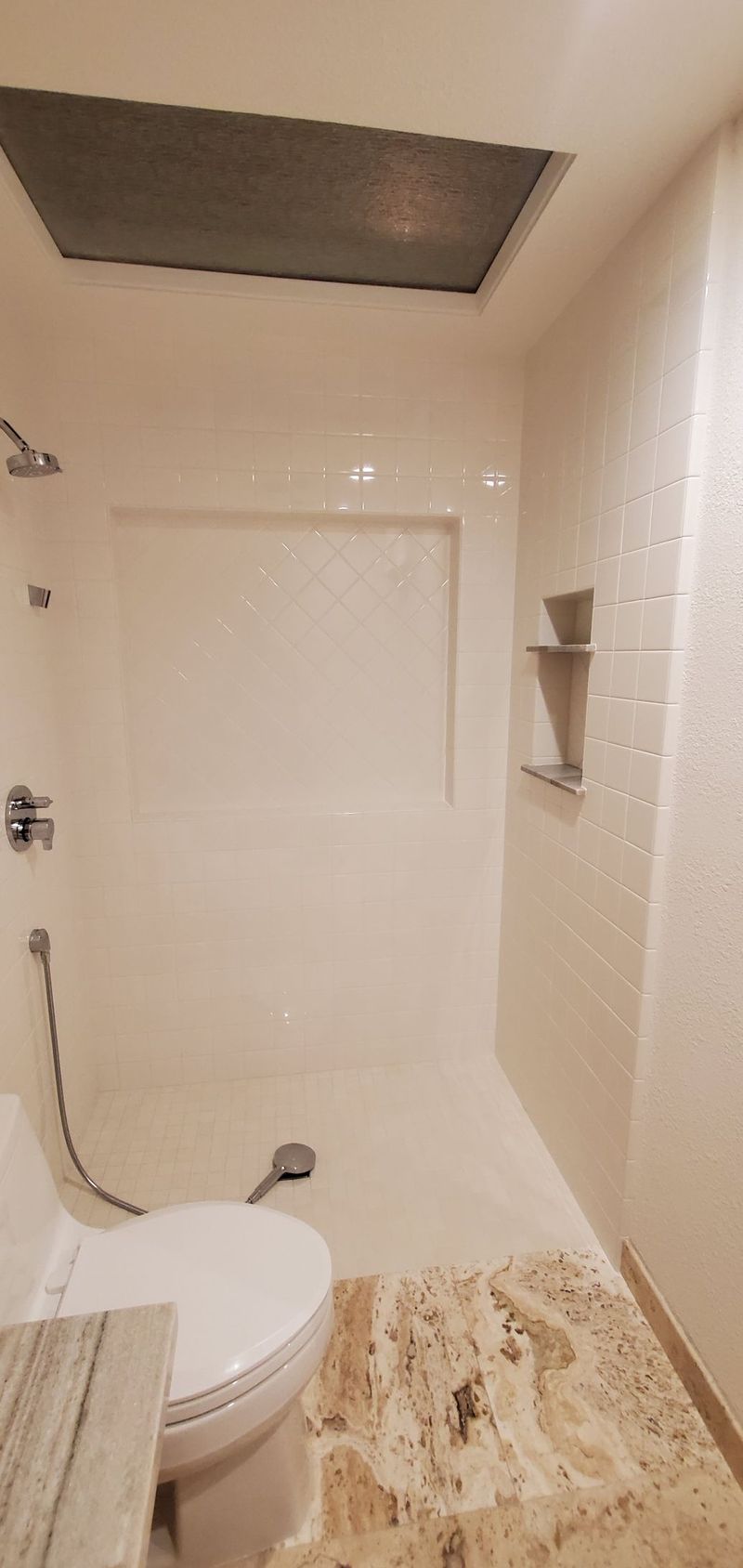 Bathroom with white walls, toilet, showerhead, and a textured floor. Recessed ceiling light.