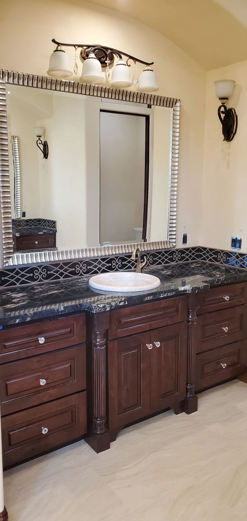 Bathroom with dark brown cabinets, a black countertop, and a large mirror.