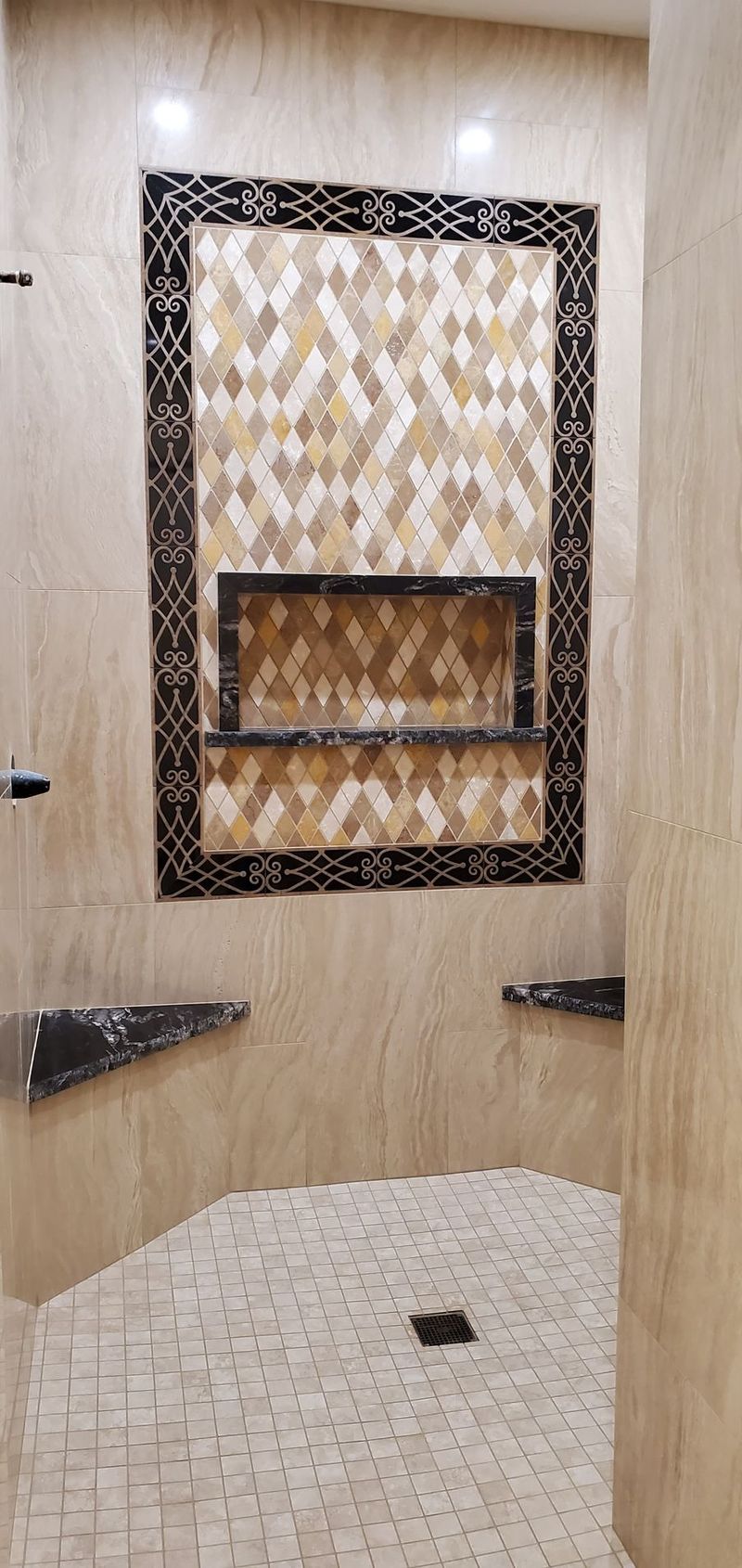 Shower with mosaic tile accent wall and built-in shelf; light stone flooring and walls.