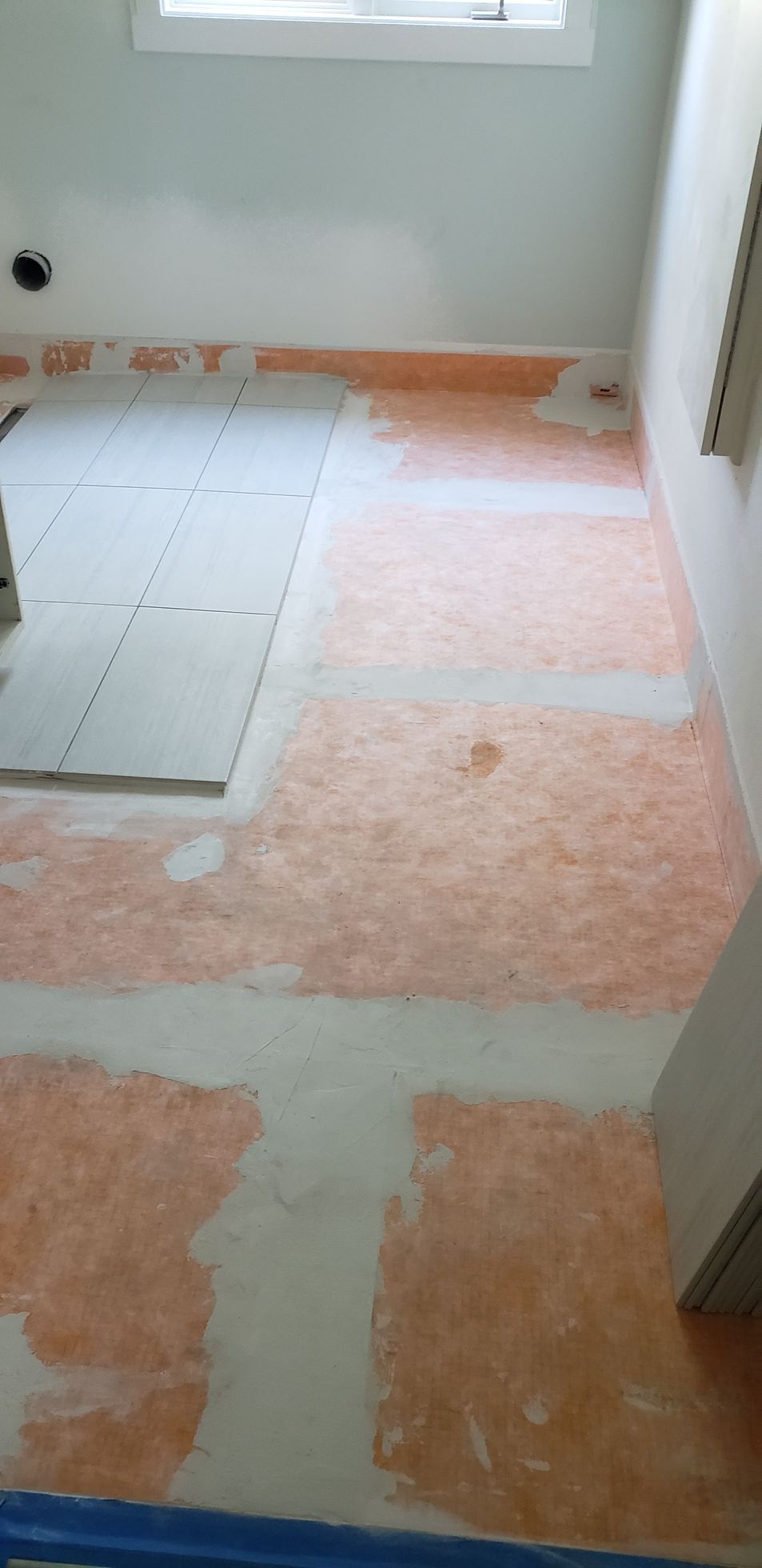 Interior construction showing an orange water membrane applied to the subfloor, with some cement board and a window.