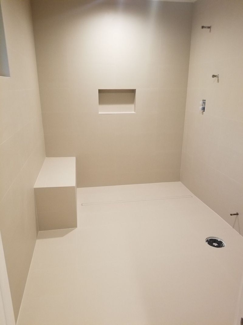 Empty shower with built-in bench and recessed shelf, light beige walls and floor, fixtures installed.