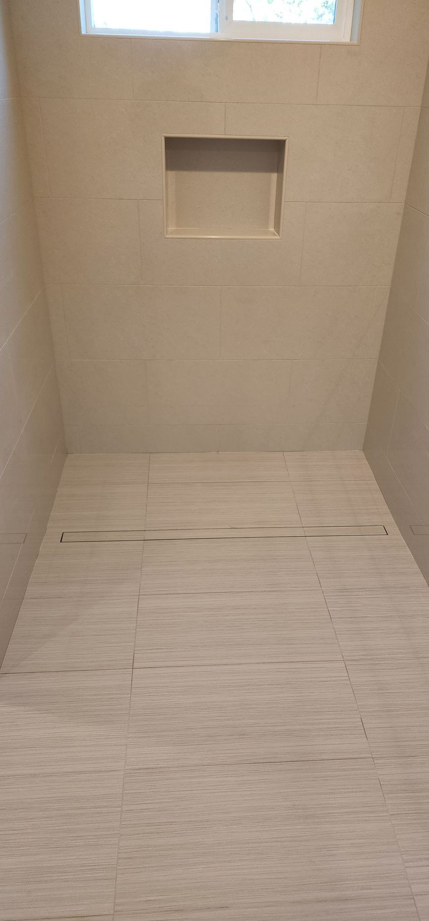 Empty shower with a small window, built-in shelf, and beige tiled walls and floor.