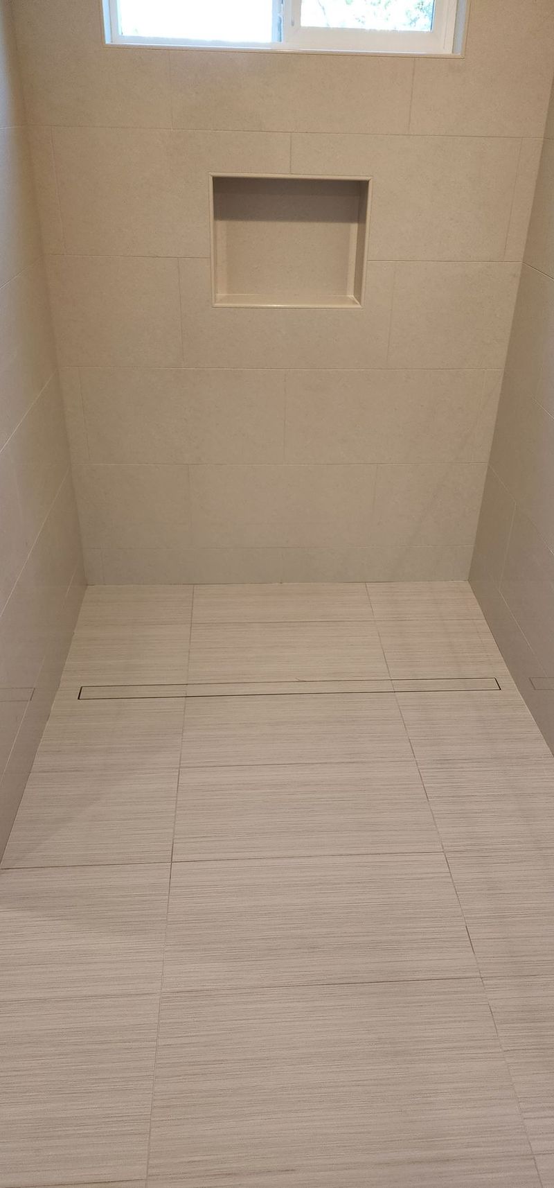 Empty shower with a small window, built-in shelf, and beige tiled walls and floor.