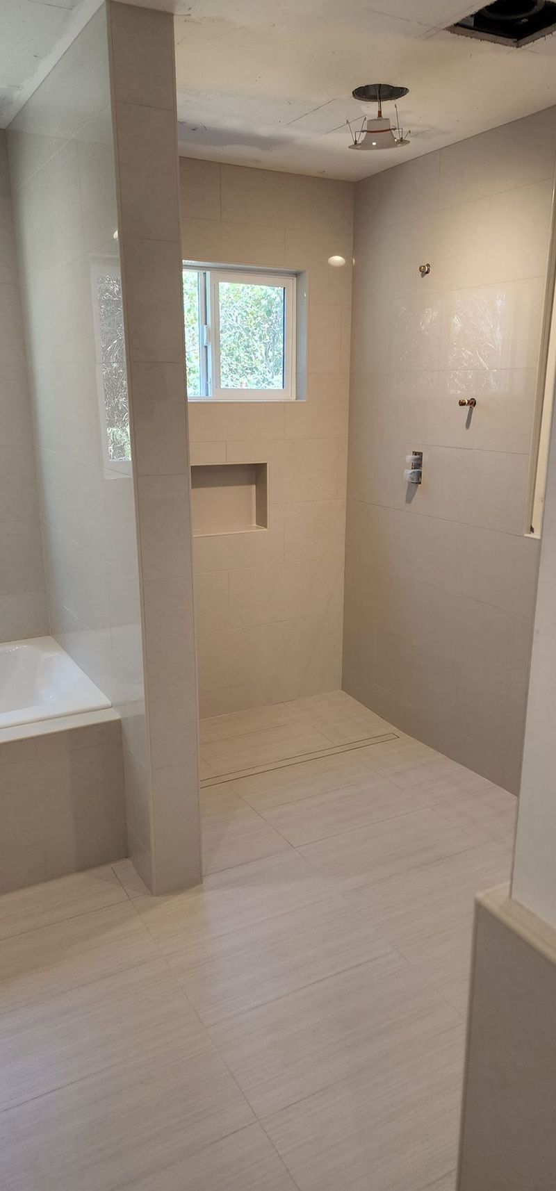 Bathroom under construction; light-colored tiles, shower area, built-in bathtub, and window.
