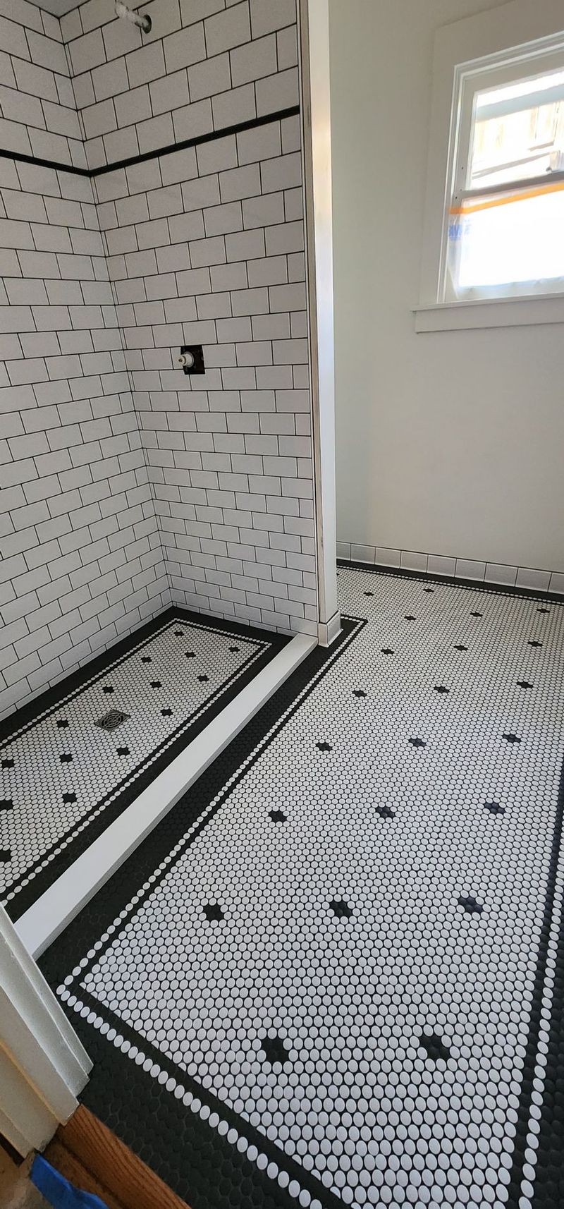 Bathroom with white and black tiled walls and floor. A window is in the background.