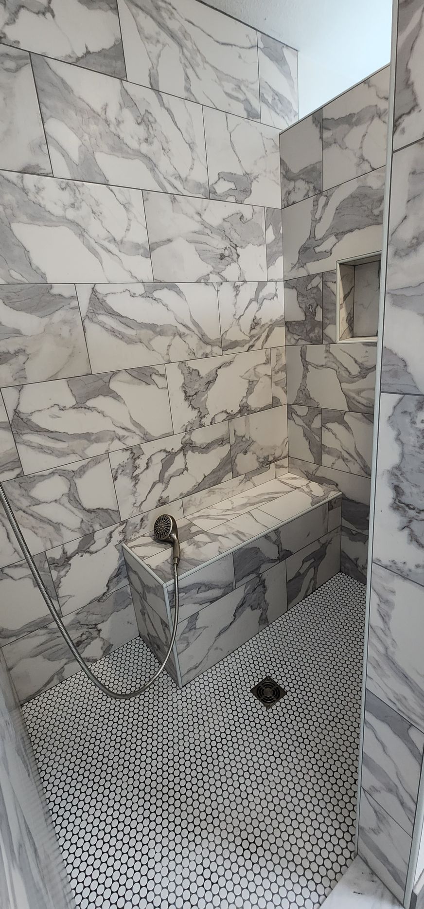 A marble-tiled shower with a built-in bench and a patterned floor.