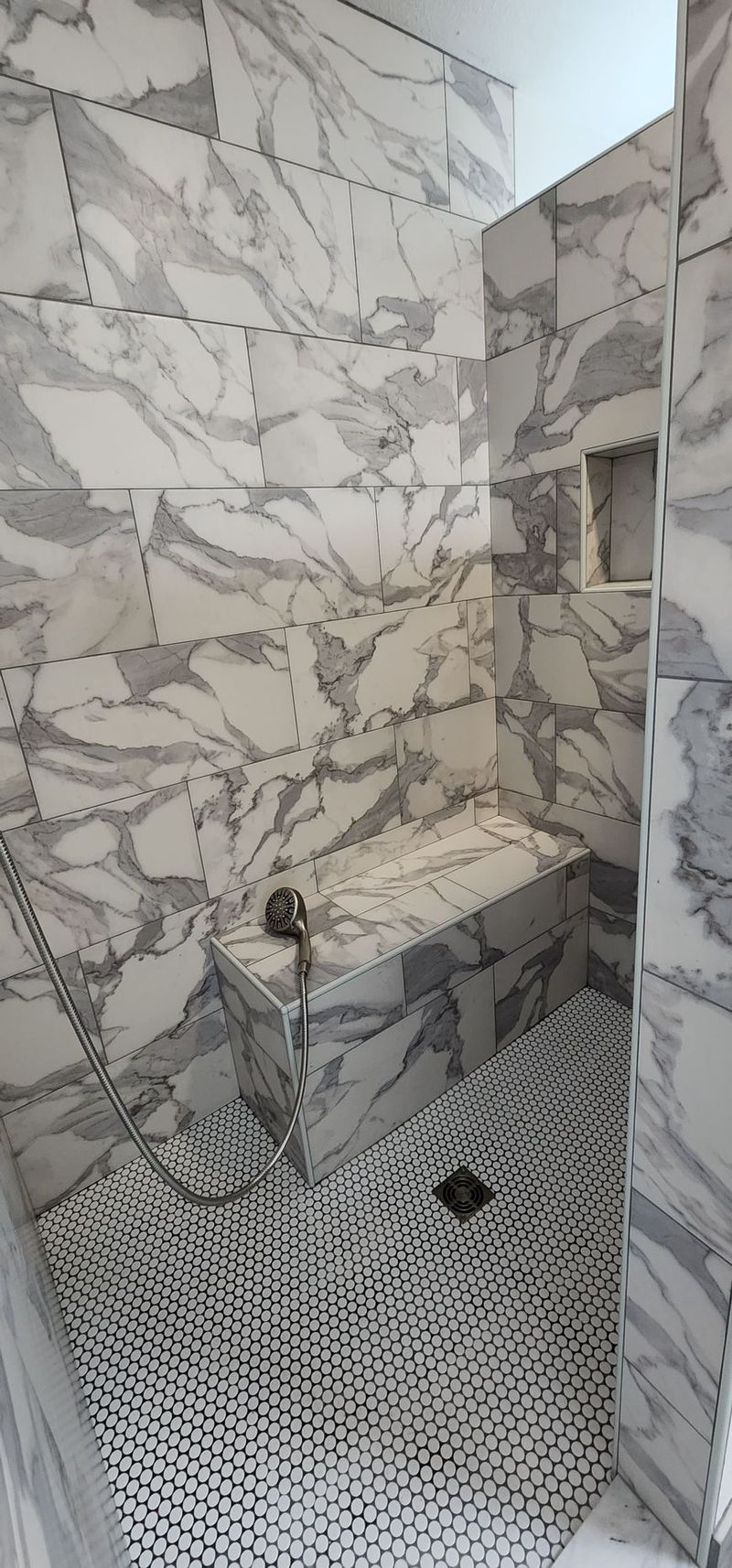 A marble-tiled shower with a built-in bench and a patterned floor.