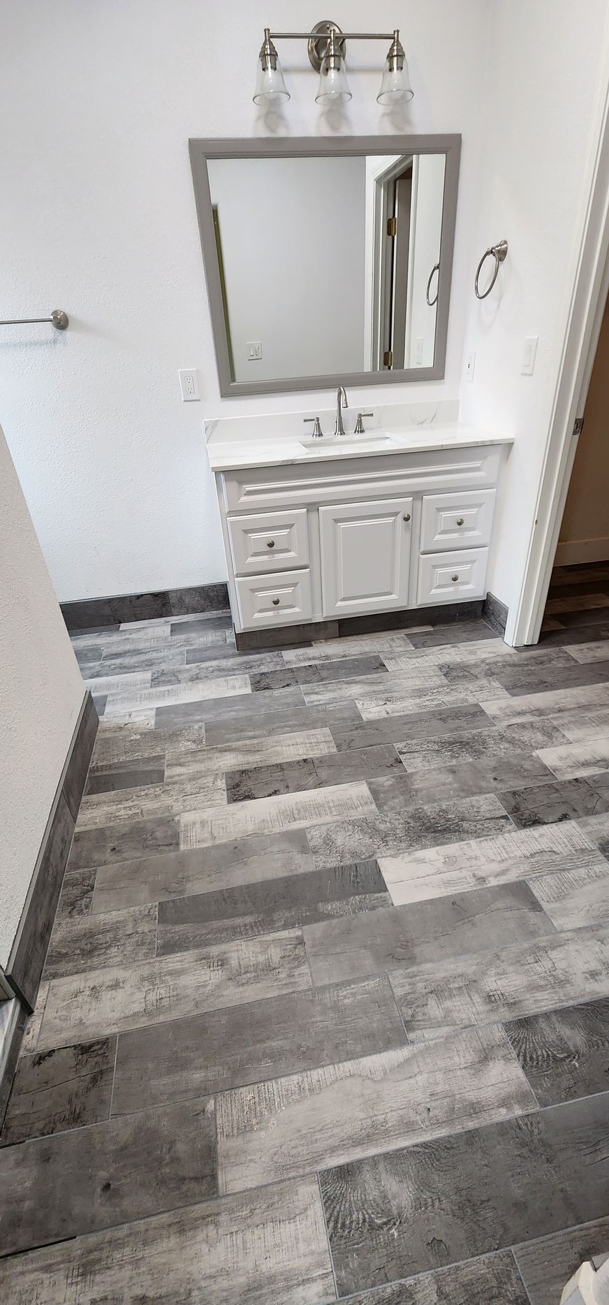 Bathroom with gray and white vanity, mirror, and wood-look tile flooring.