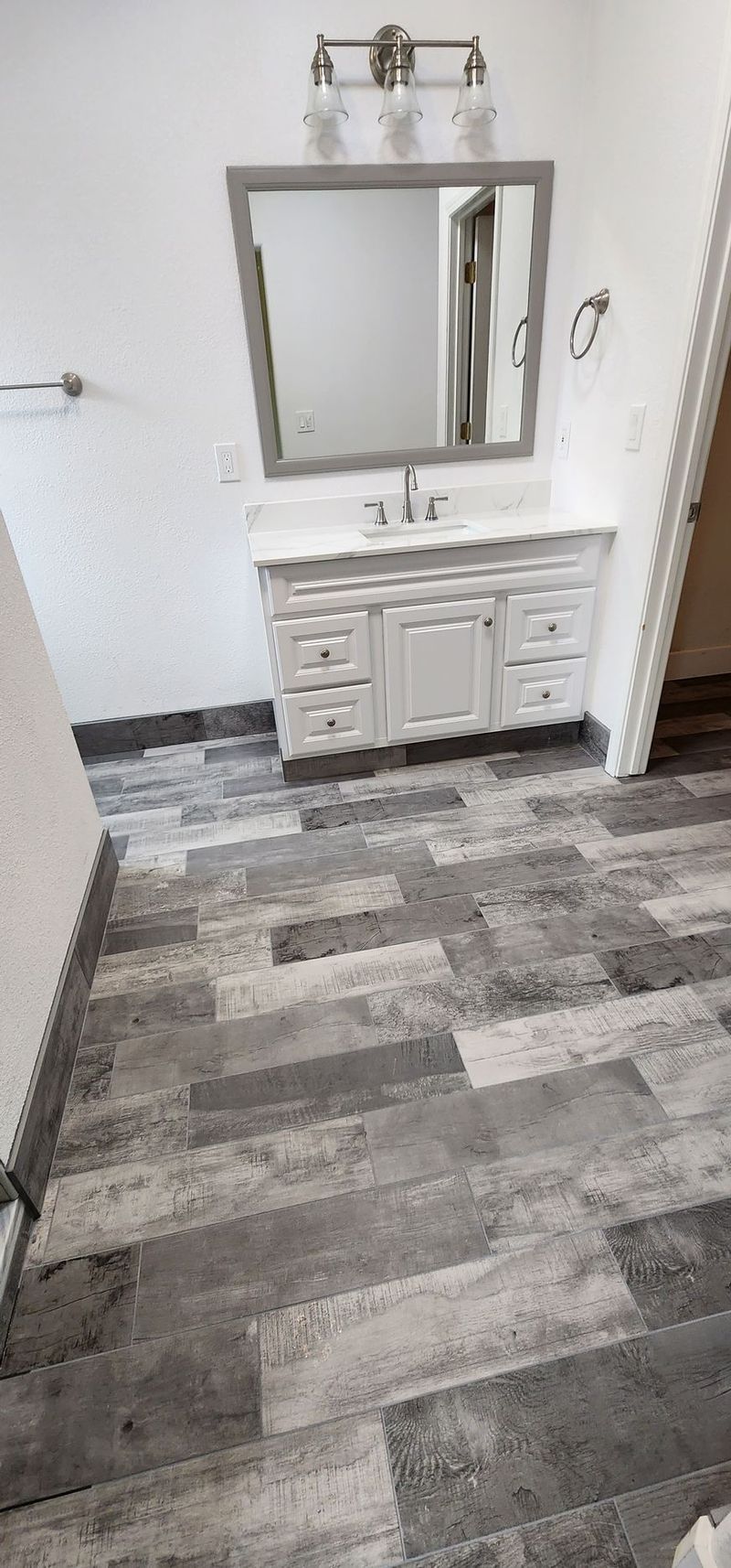 Bathroom with gray and white vanity, mirror, and wood-look tile flooring.