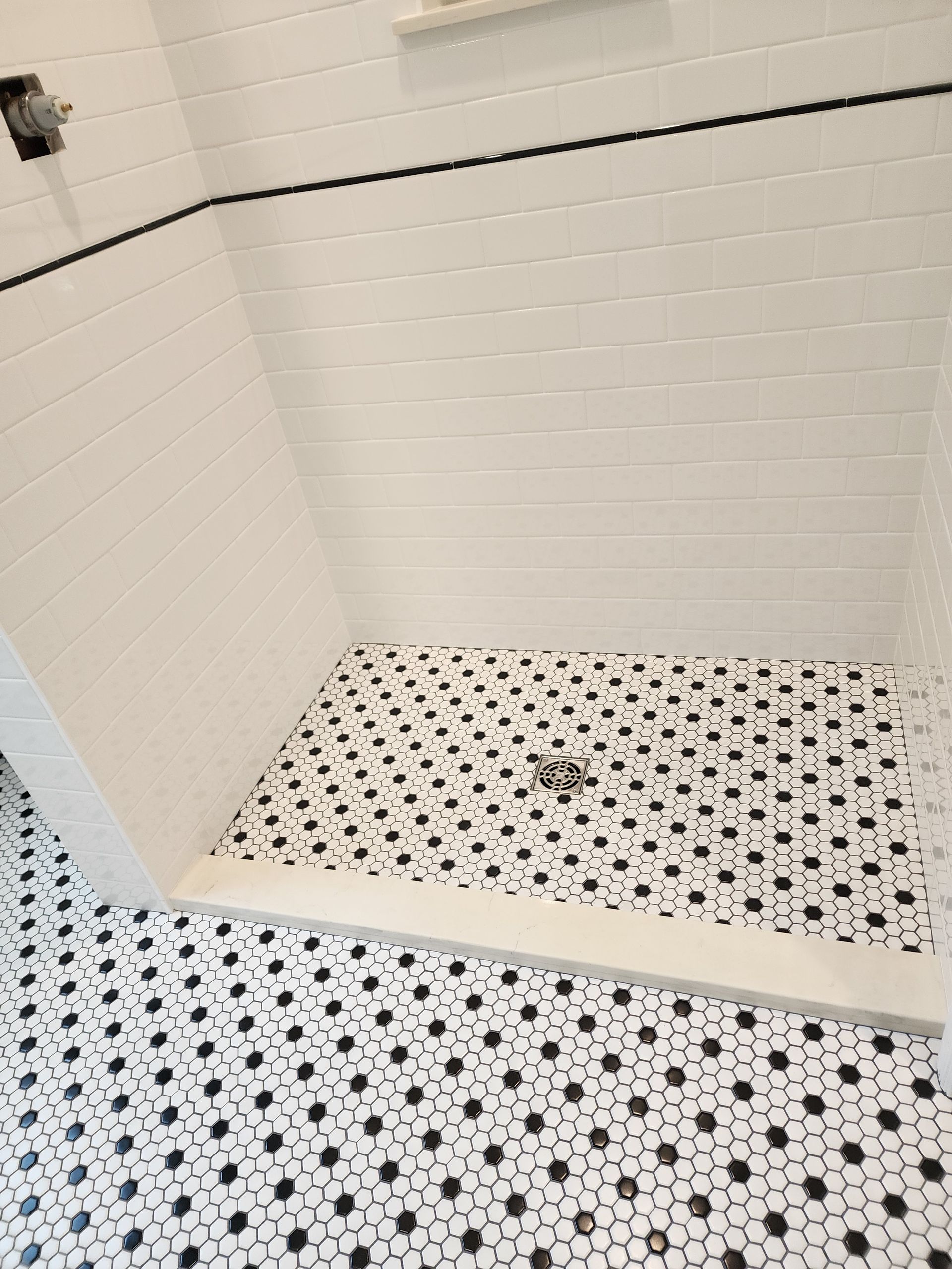 White tile shower with black hexagonal floor tiles.