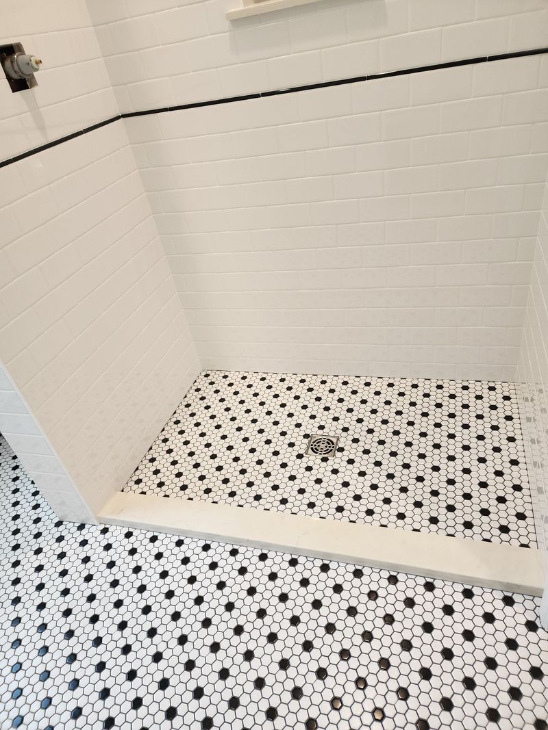 White tile shower with black hexagonal floor tiles.