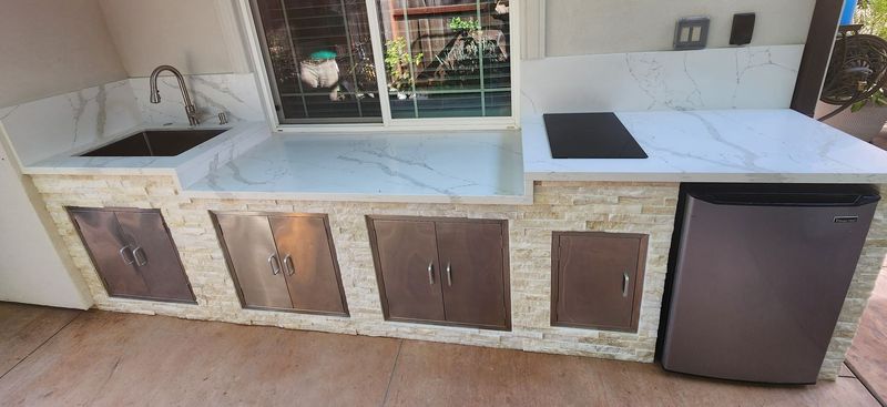 Outdoor kitchen with a sink, countertop, cabinets, and a mini-fridge.