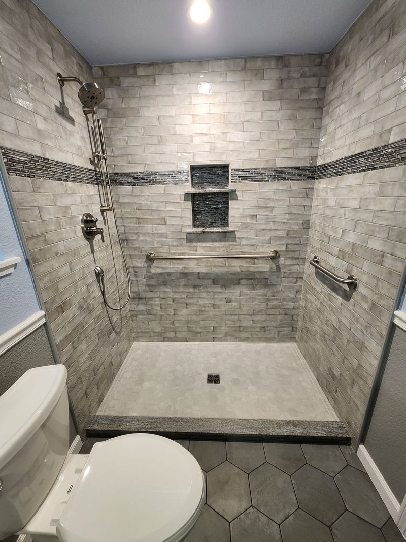 Newly renovated shower with stone tile, built-in shelves, and grab bars. Gray and silver tones dominate.