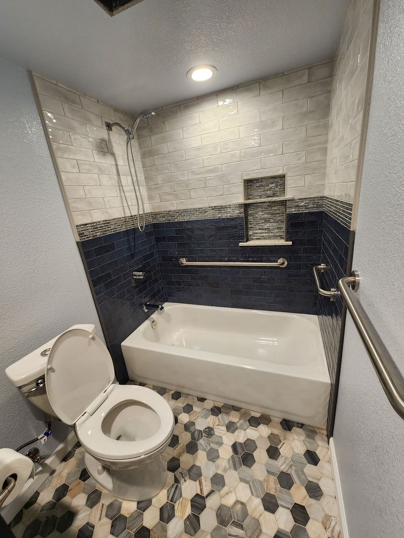 Bathroom with a white bathtub, toilet, and mosaic tile flooring and walls.