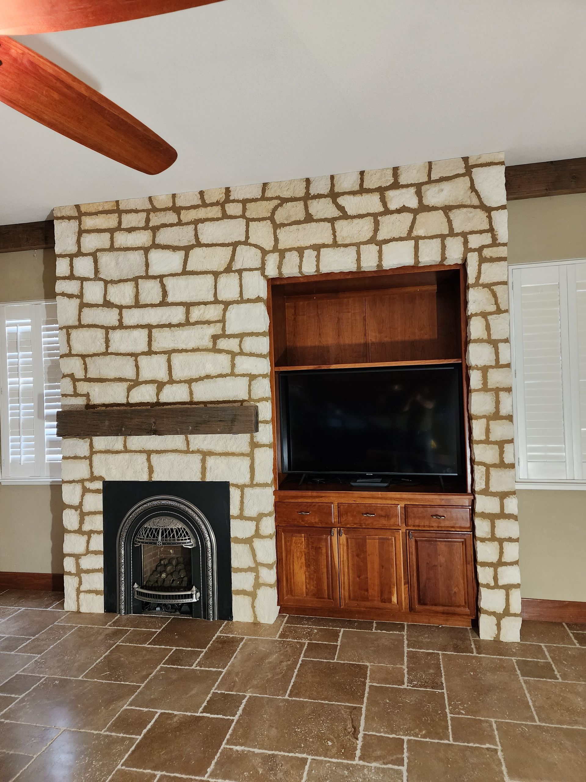 Stone fireplace with built-in wooden entertainment center and TV; brown tile floor.