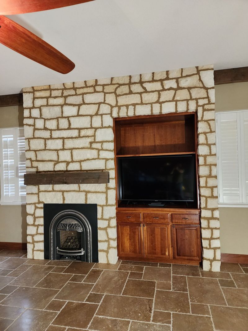 Stone fireplace with built-in wooden entertainment center and TV; brown tile floor.