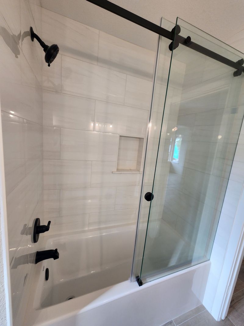 Bathroom with a white bathtub, glass sliding door, and black fixtures.