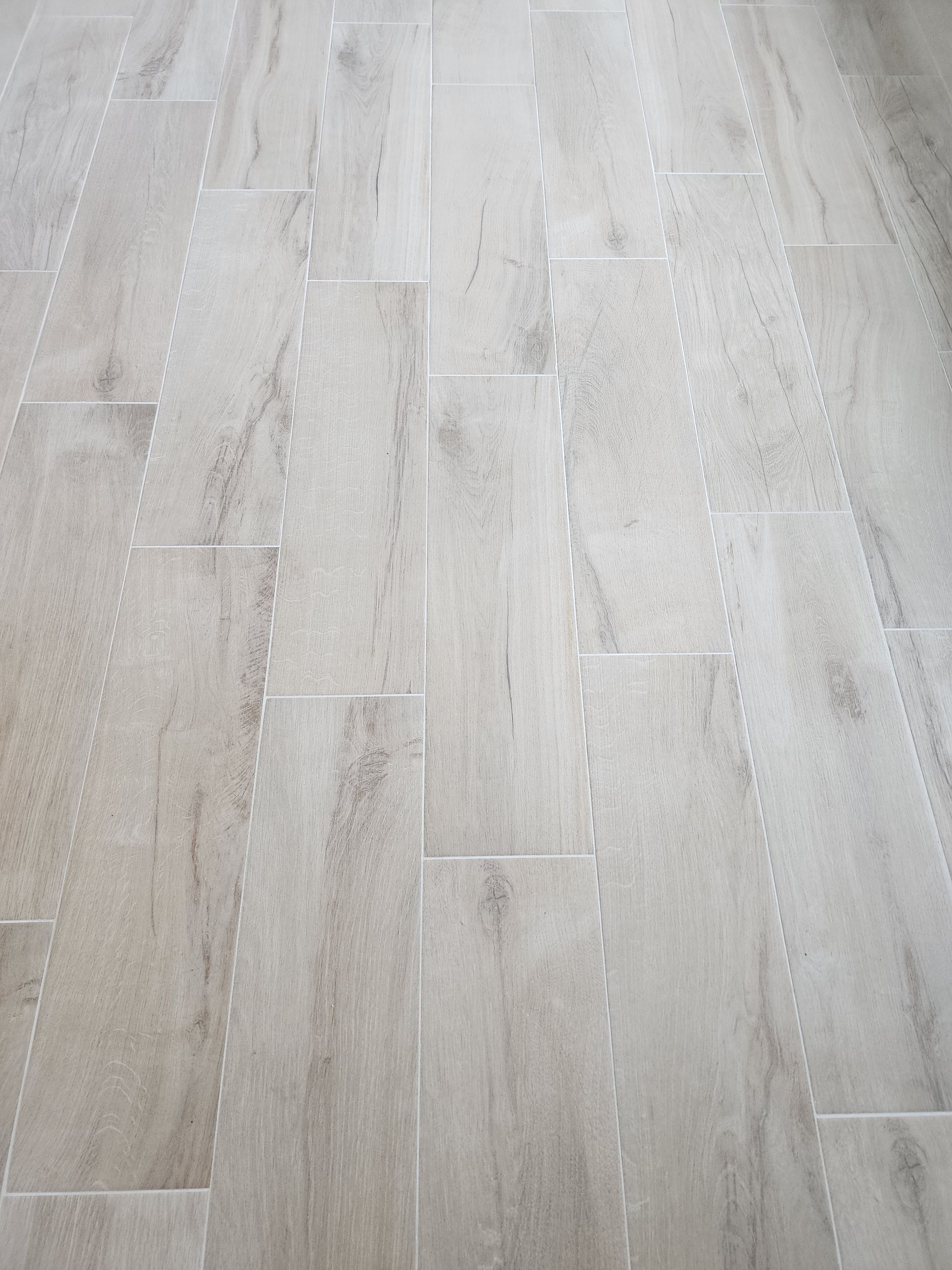 Light-colored rectangular tile floor with wood grain pattern, grout lines visible.