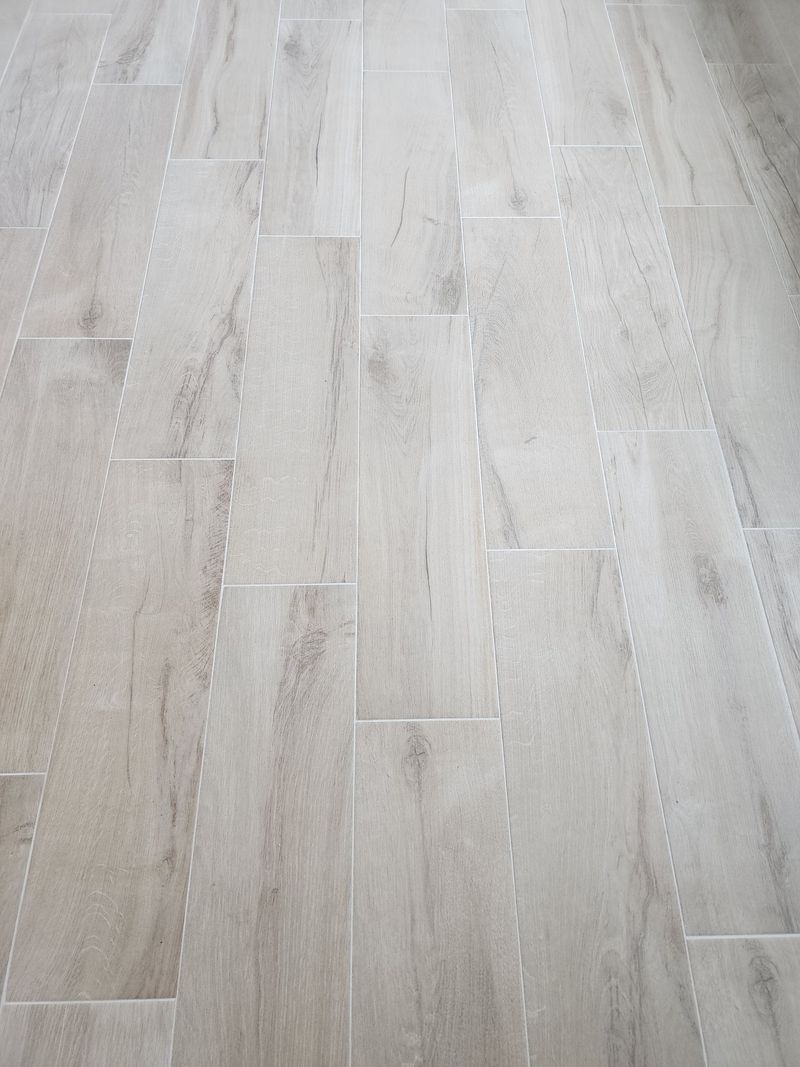 Light-colored rectangular tile floor with wood grain pattern, grout lines visible.