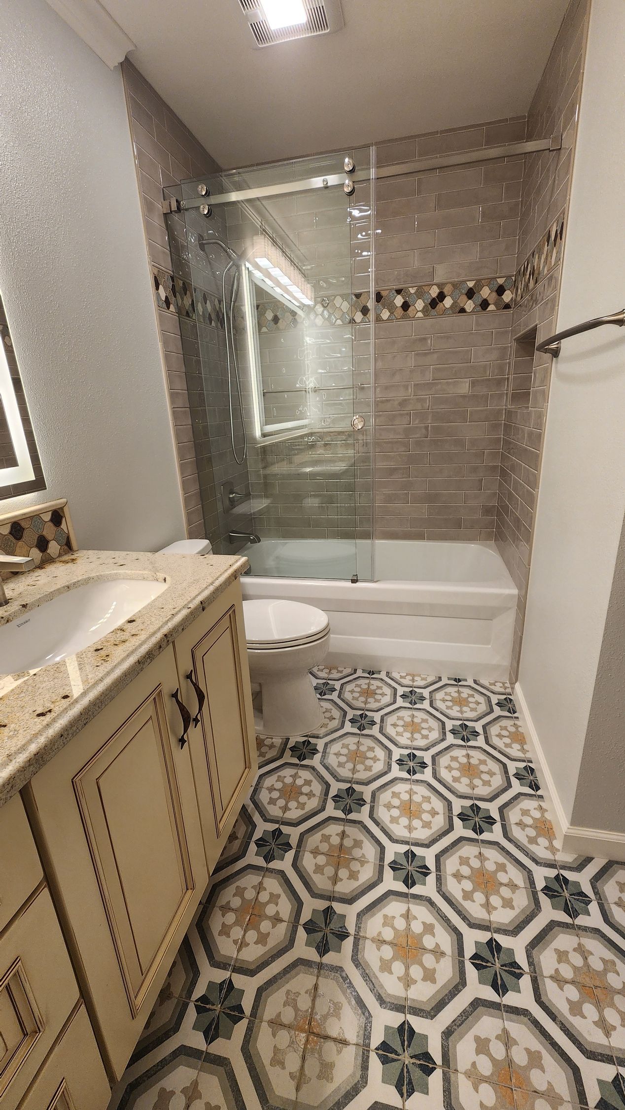 Bathroom with patterned floor tiles, stone wall tiles, glass shower door, and cream vanity.
