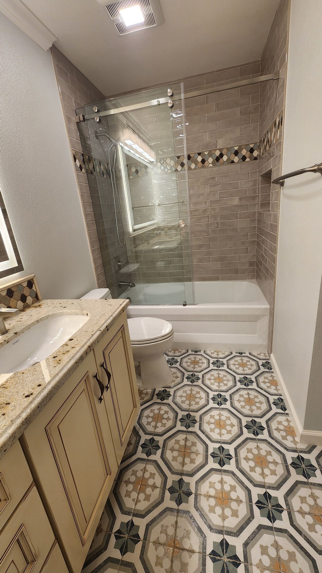 Bathroom with patterned floor, vanity, toilet, and tiled shower/bath area.