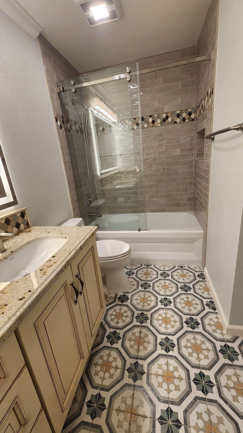 Bathroom with patterned floor, vanity, toilet, and tiled shower/bath area.