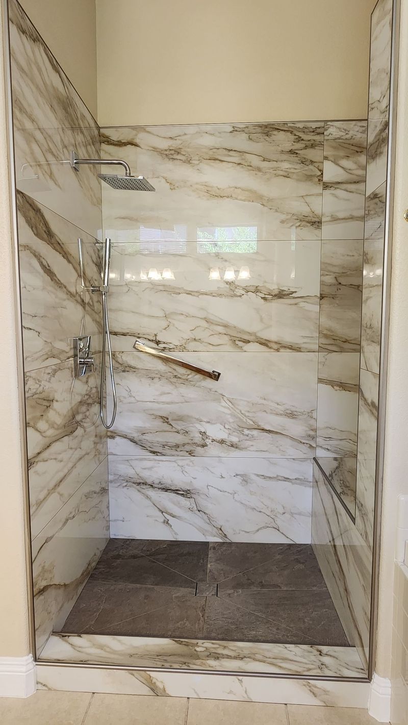 Walk-in shower with marble-like walls and a stone floor; chrome fixtures are visible.