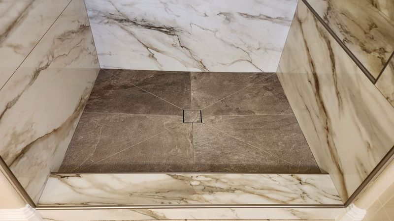 Shower stall with marble walls and a textured tile floor, featuring a centered drain.