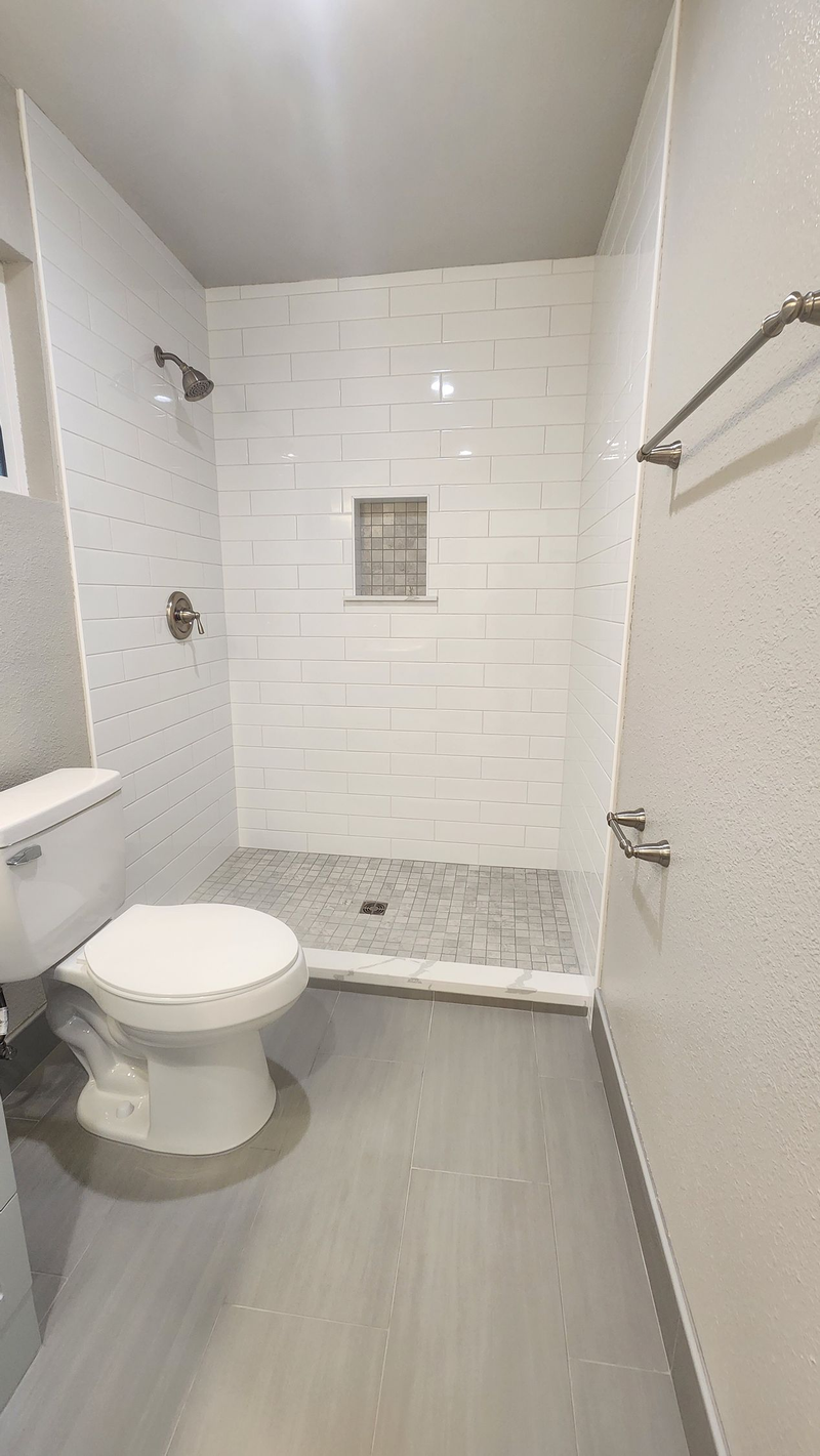Modern bathroom with white textured tile shower and walls, gray floor, toilet.