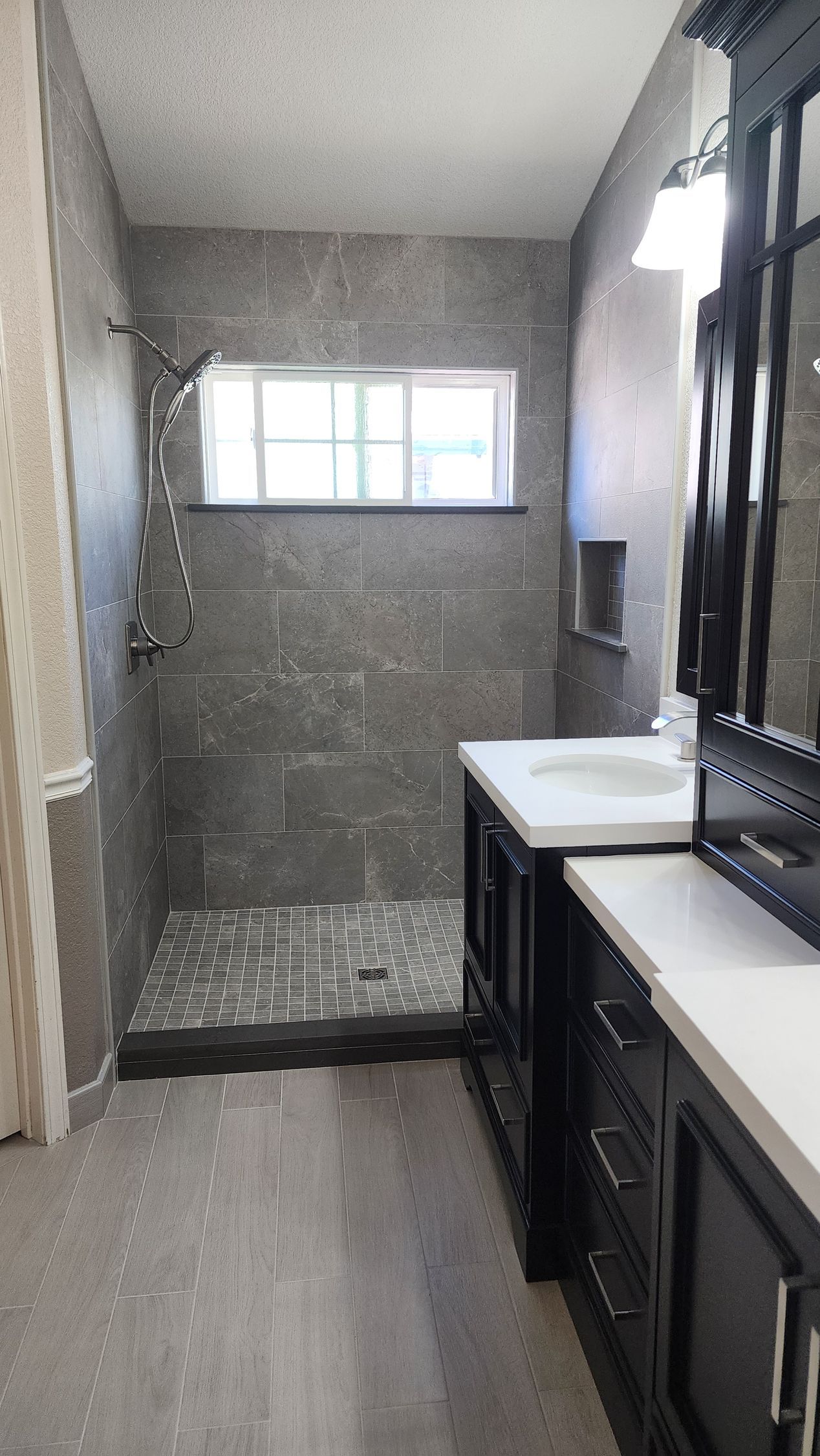 Bathroom with gray tiled shower, window, and black vanity with white countertop.