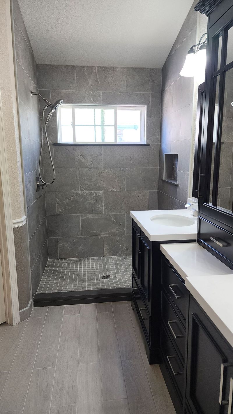 Bathroom with gray tiled shower, window, and black vanity with white countertop.