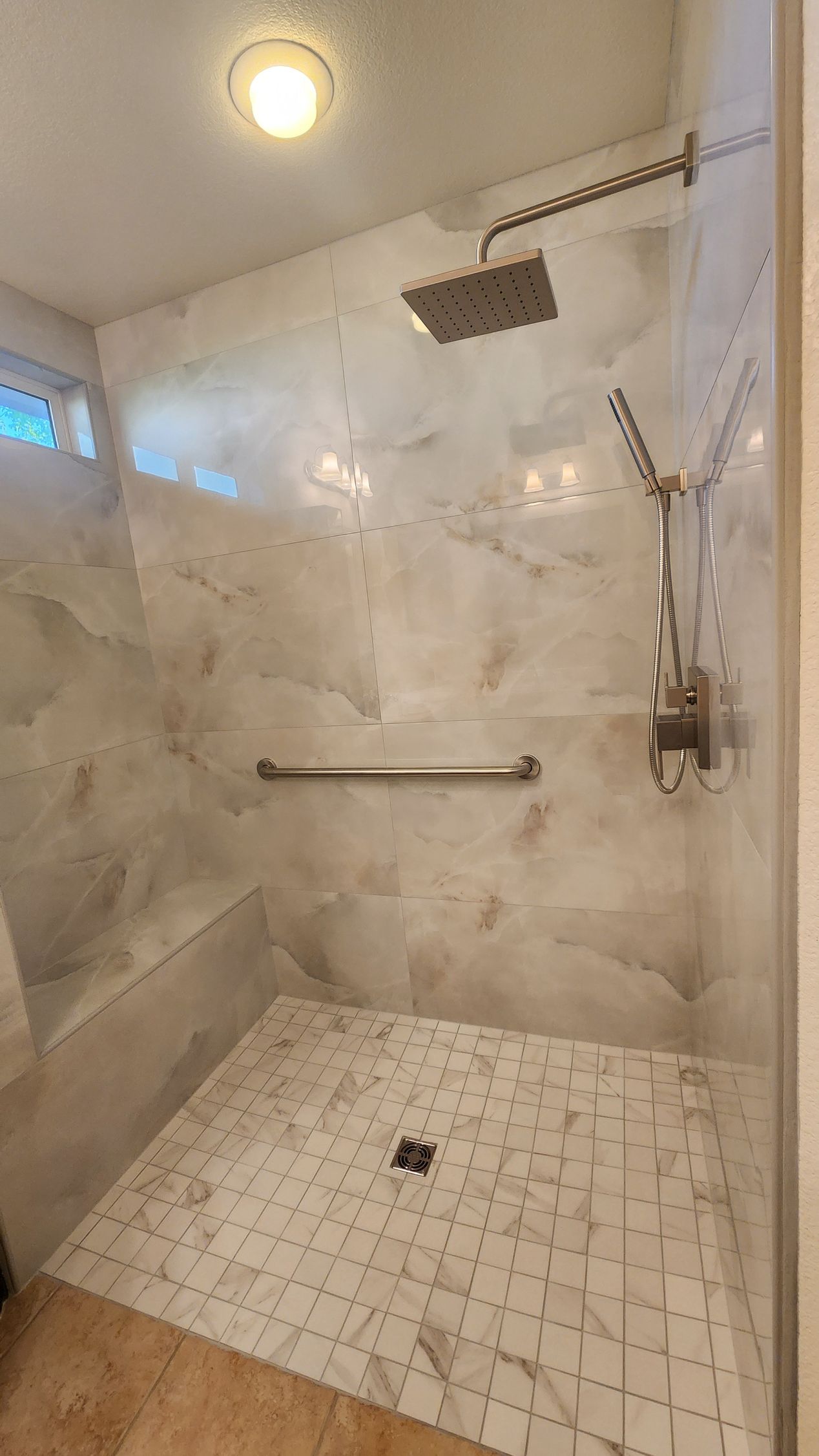 Walk-in shower with marble-look walls and floor, shower head, hand-held shower, and grab bar.