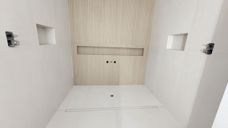 Empty, white room under construction; wood-paneled wall, square niches, electrical outlets visible.