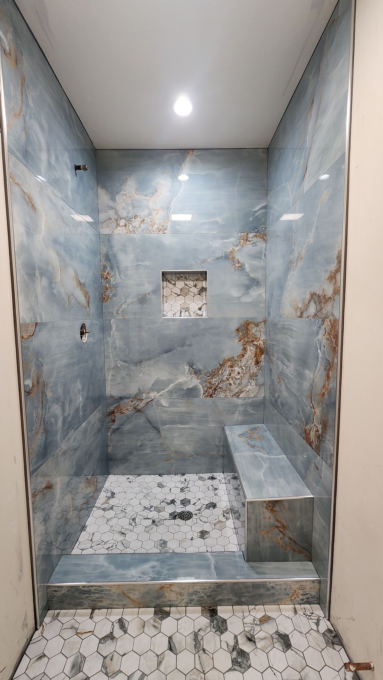 Blue and brown tiled shower with built-in bench, recessed shelf, and patterned floor tiles.