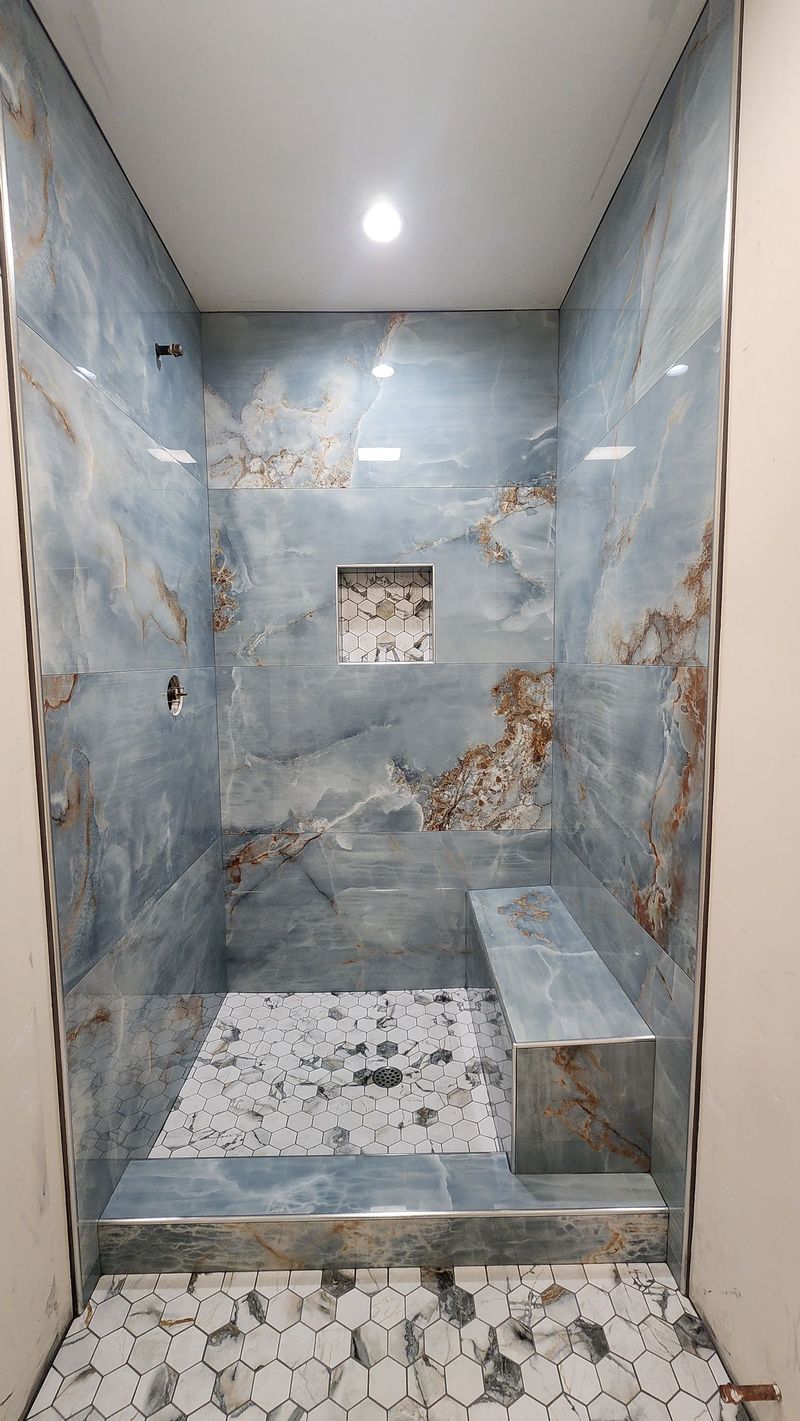 Blue and brown tiled shower with built-in bench, recessed shelf, and patterned floor tiles.