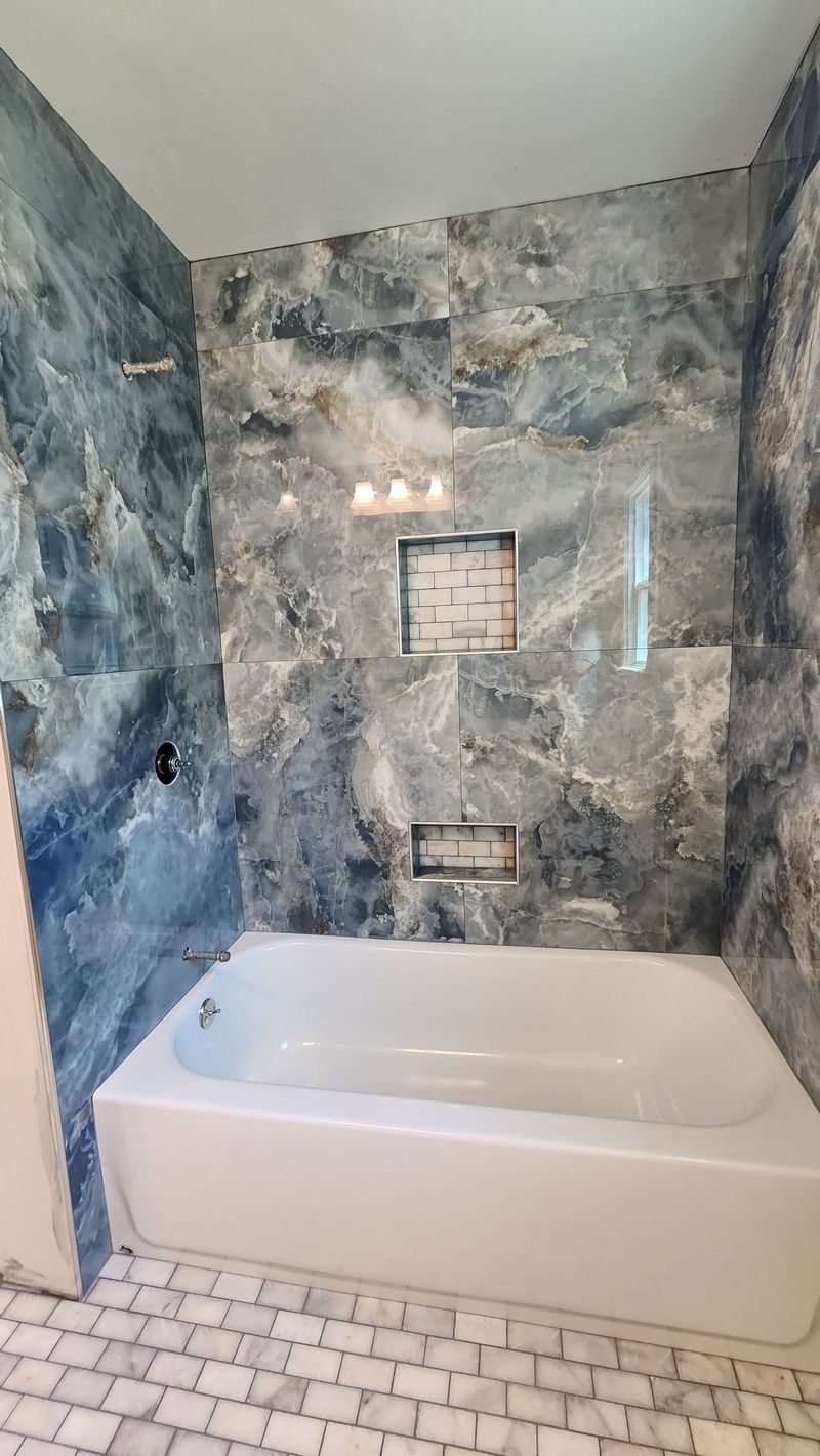 Bathroom with a white bathtub and blue-gray tiled walls.