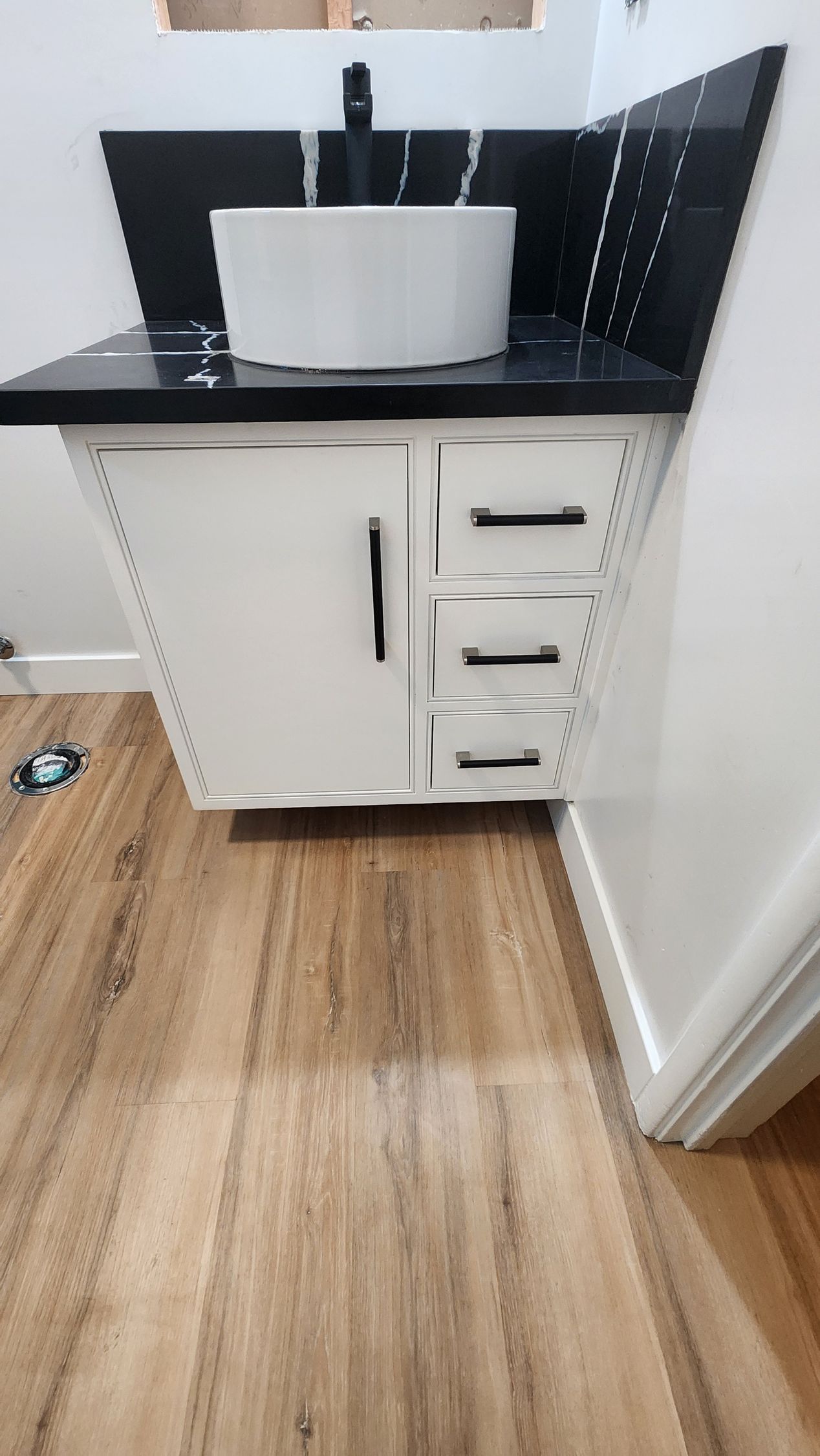 White bathroom vanity with black countertop and fixtures, against a tiled wall.