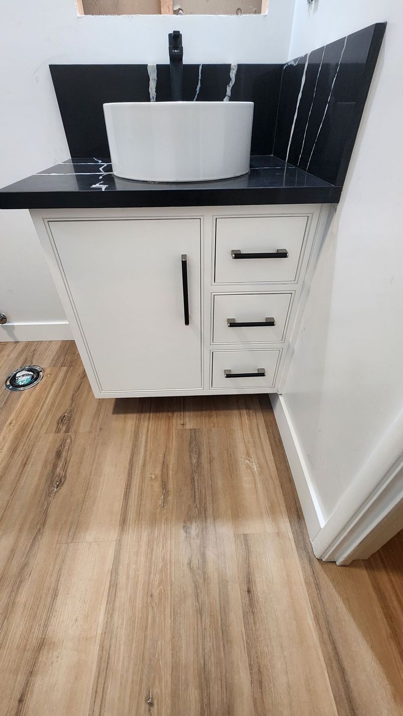 White bathroom vanity with black countertop and fixtures, against a tiled wall.