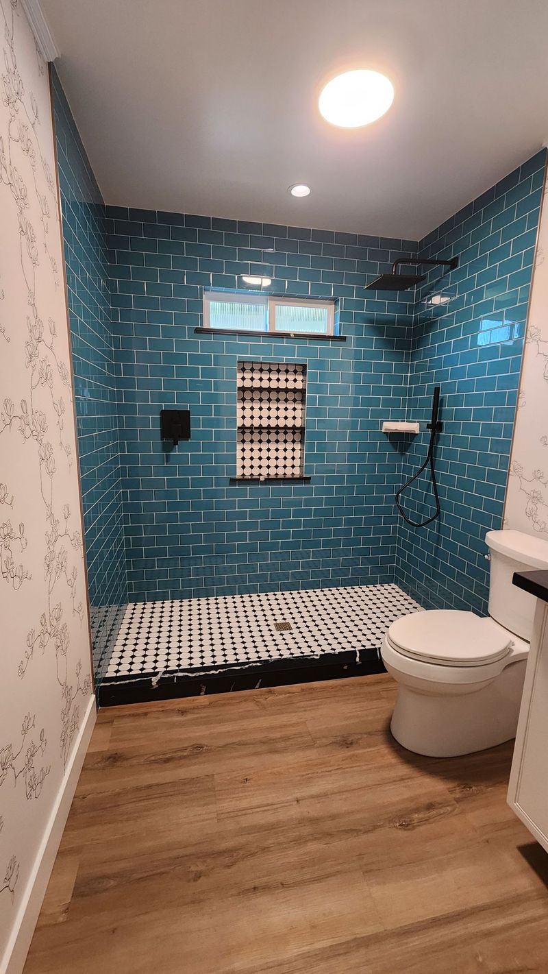 Modern bathroom with turquoise tiled shower, white toilet, and wood-look flooring.