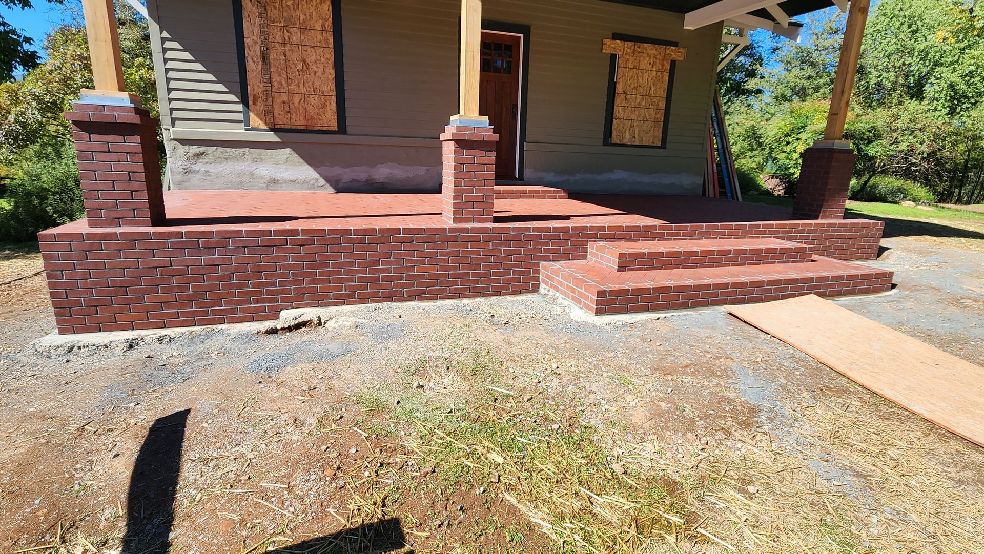 A house with a brick porch and steps, windows boarded up, and a wooden ramp.