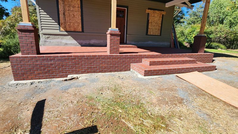 A house with a brick porch and steps, windows boarded up, and a wooden ramp.