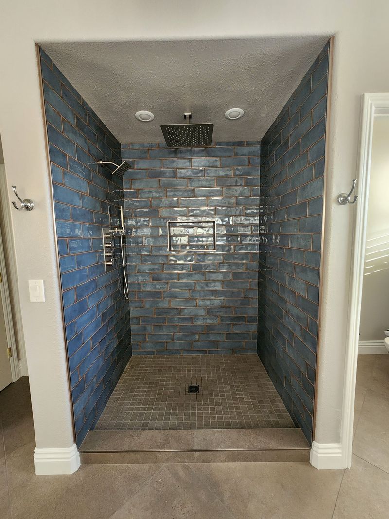 Blue tiled shower stall with rain shower head and fixtures.