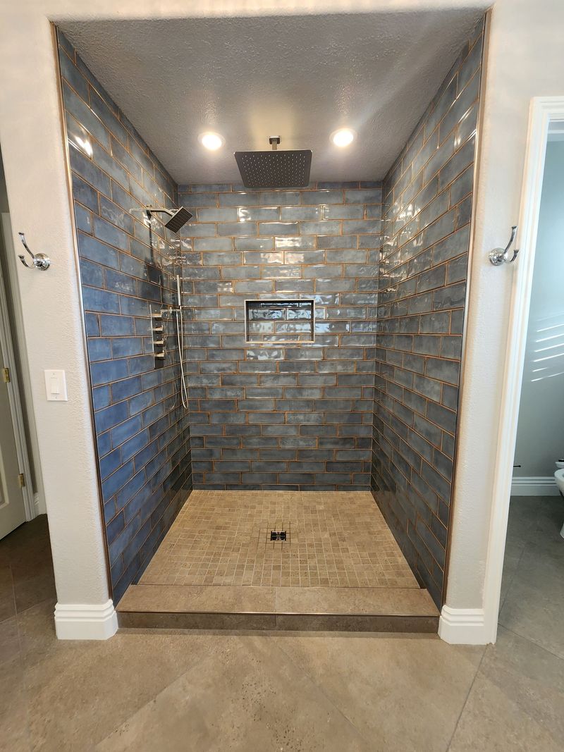 Shower with dark blue-gray tiled walls, brown floor, and built-in shelf.
