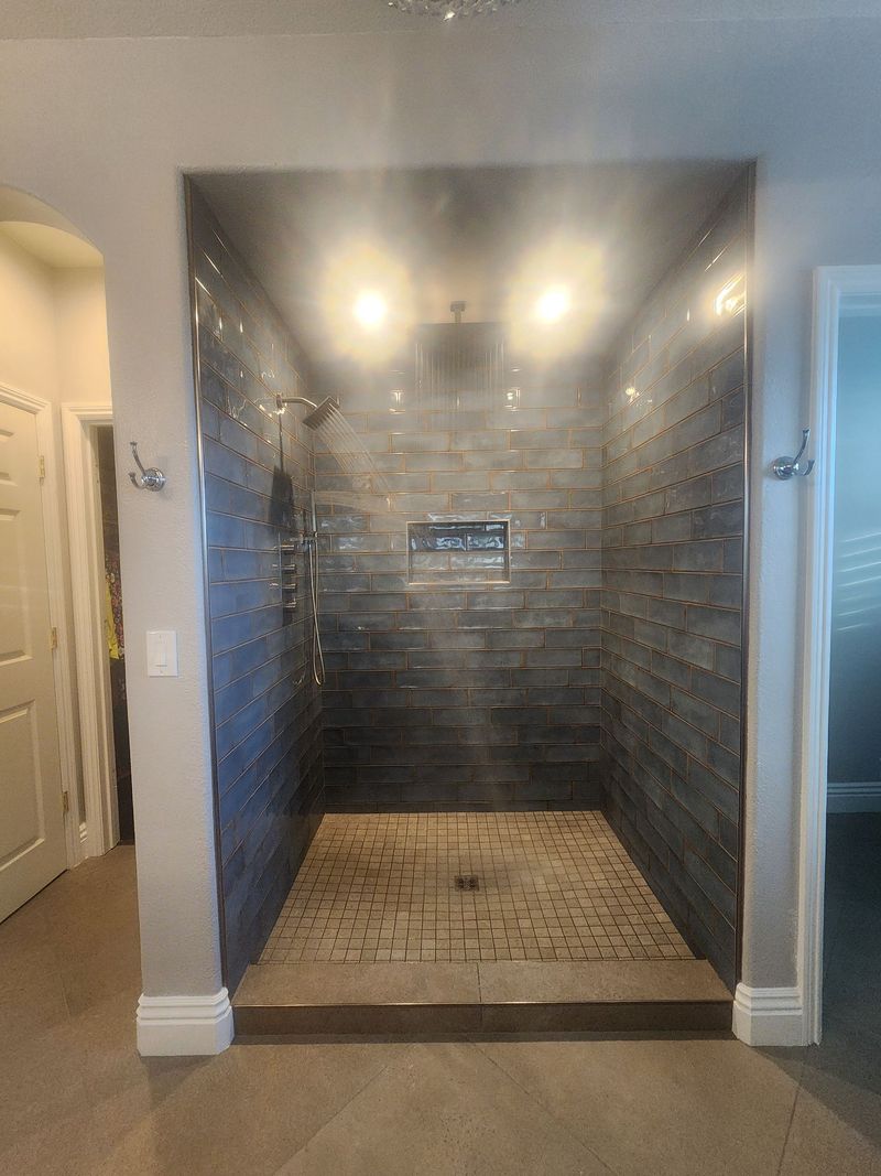 Walk-in shower with dark gray tiled walls and floor, and chrome fixtures.
