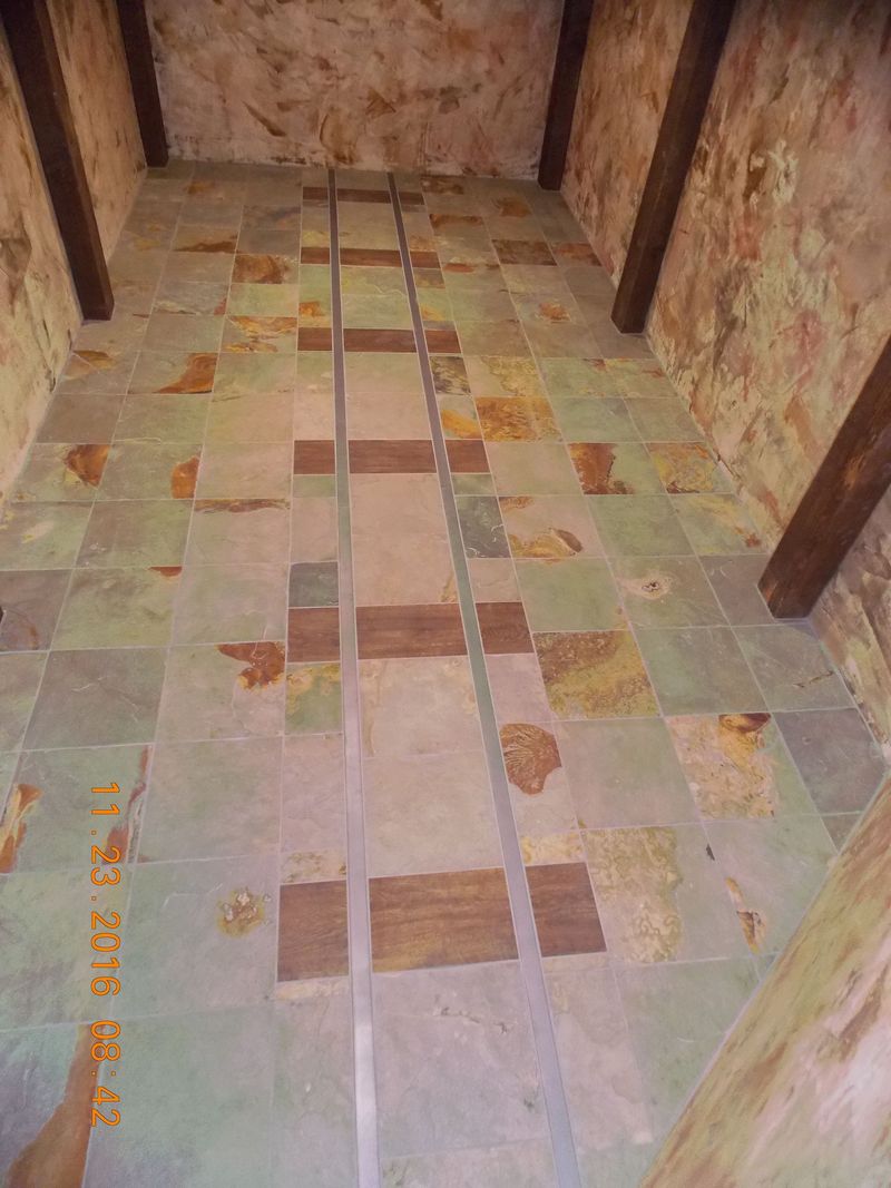Interior view: stone tiled floor with a central strip, bordered by wooden beams and rustic walls.