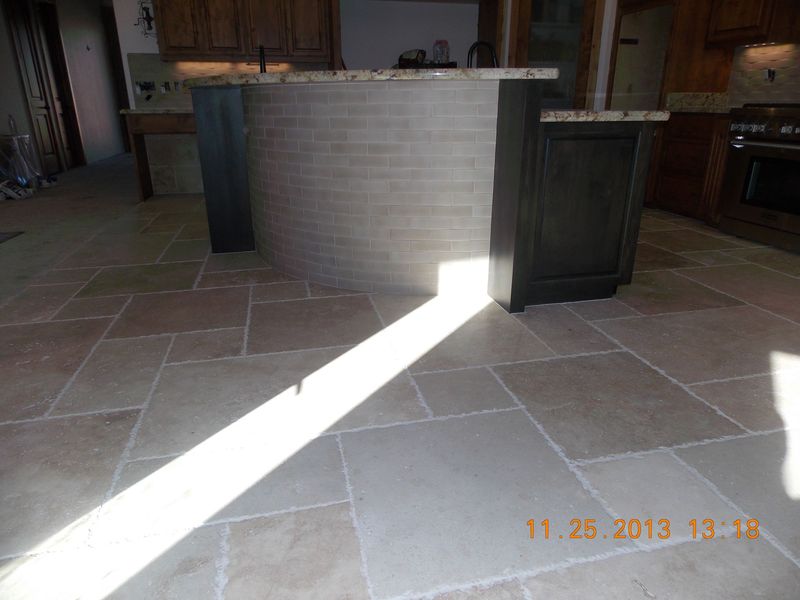 Kitchen with tiled floor, dark cabinets, island with light stone facade, sunlight across floor.