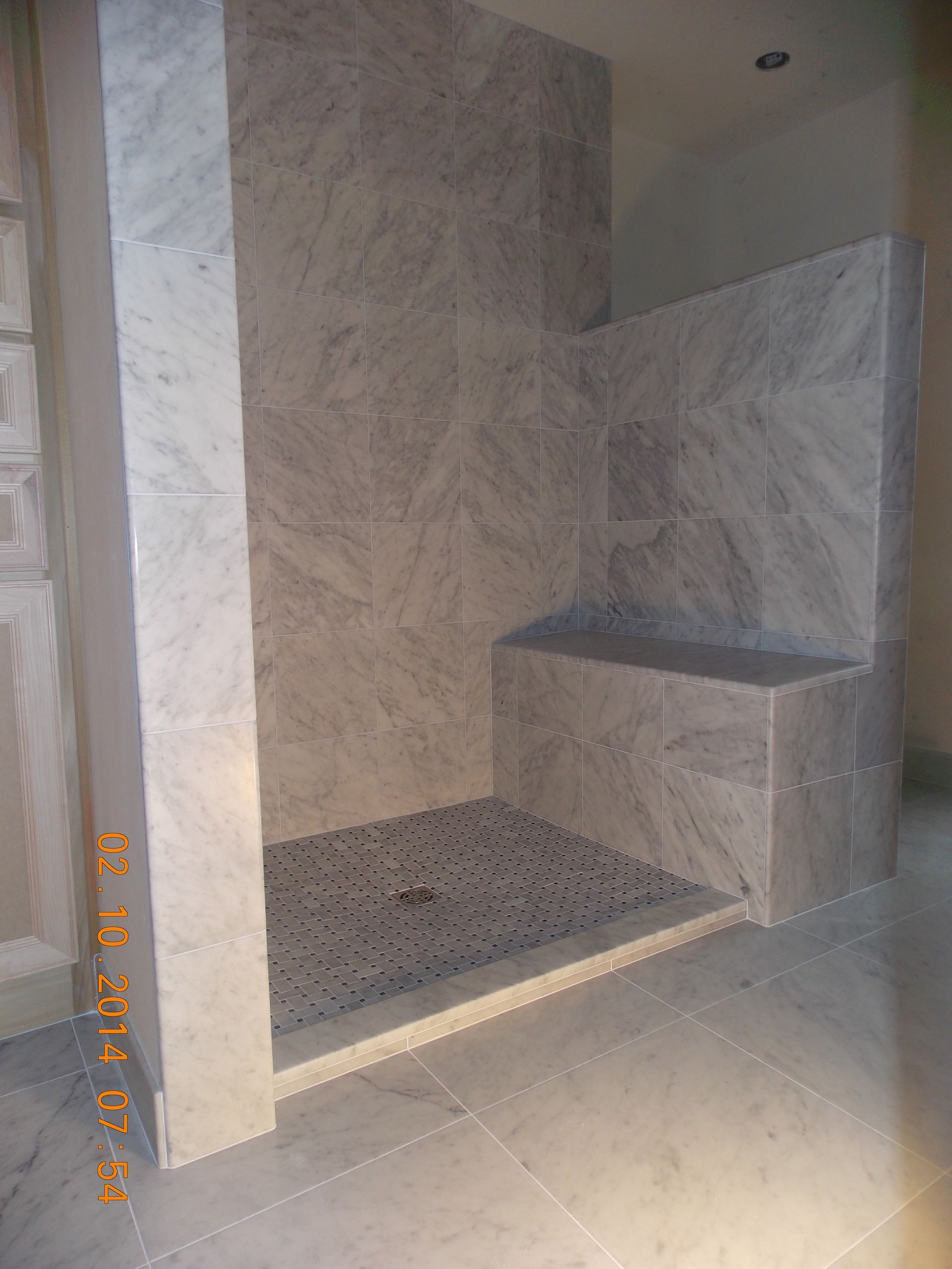 Marble-tiled shower with a built-in bench. The shower floor is covered in small, dark stones.