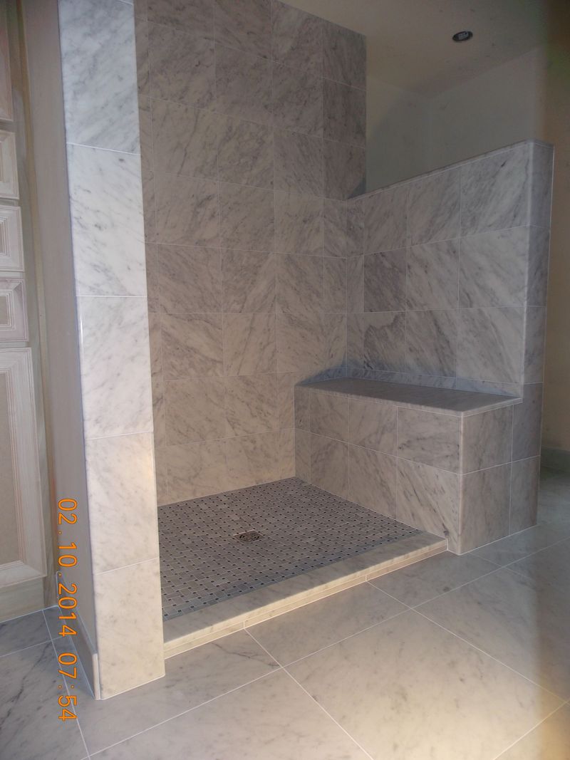 Marble-tiled shower with a built-in bench. The shower floor is covered in small, dark stones.