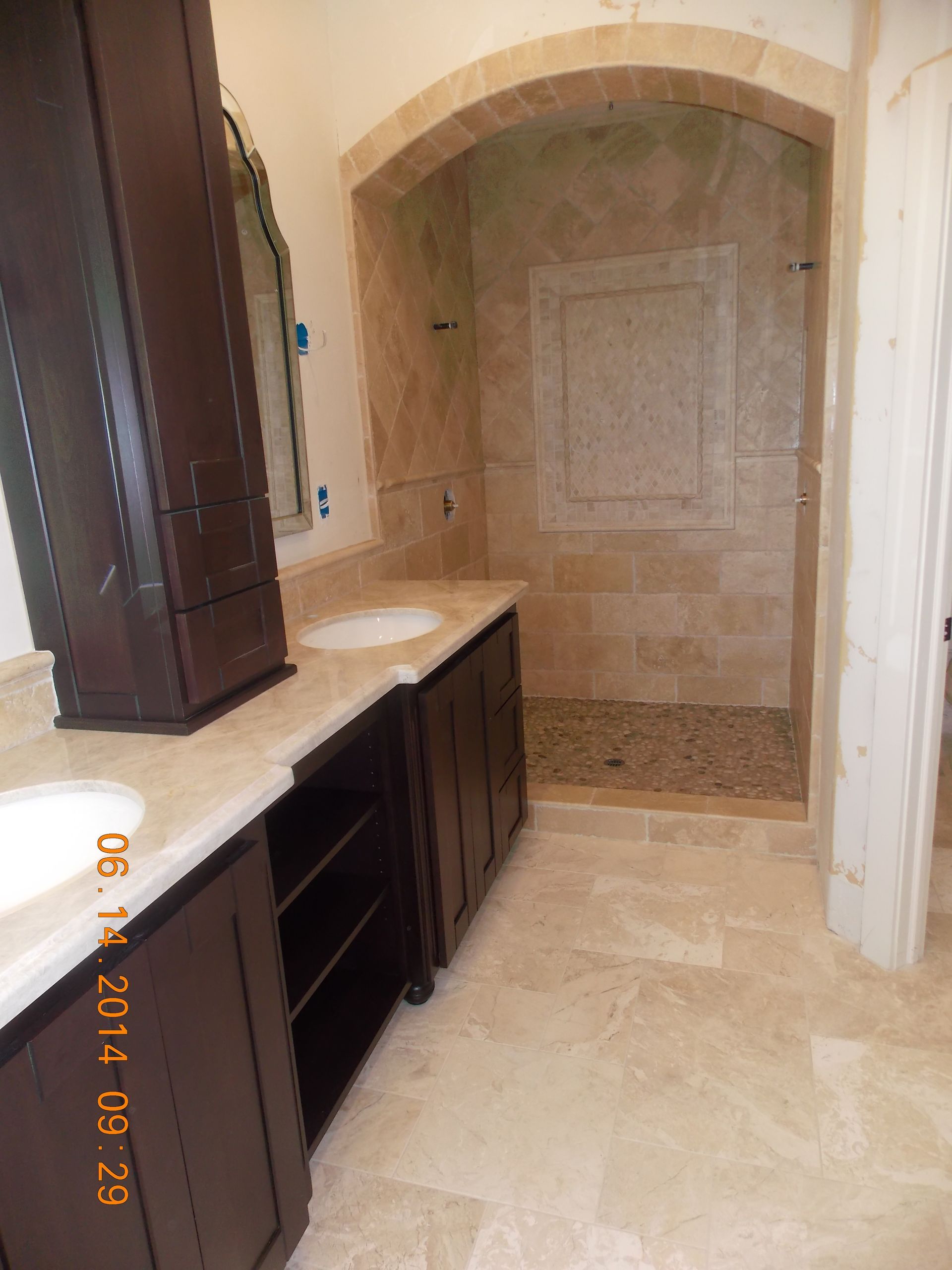 Bathroom with dark brown cabinetry, beige countertops, and a tiled shower with a pebble floor.