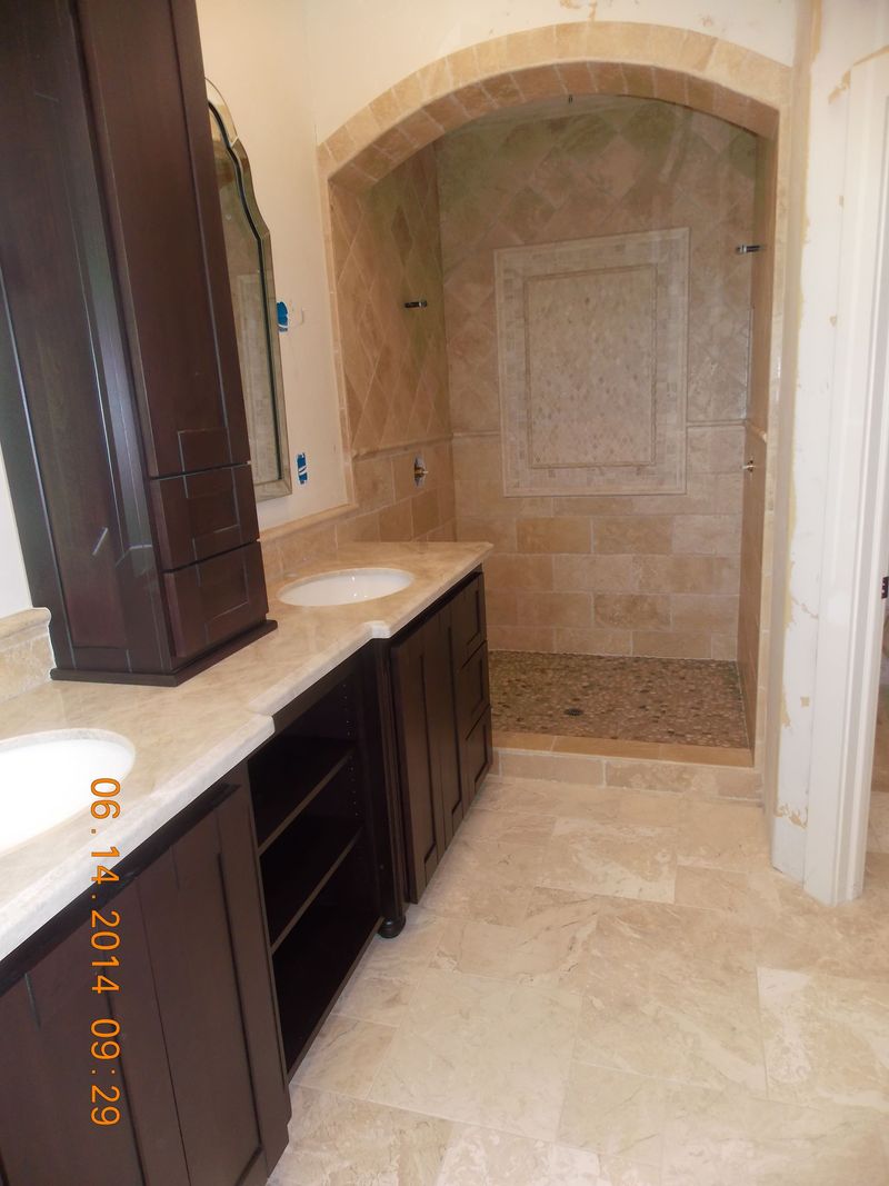 Bathroom with dark brown cabinetry, beige countertops, and a tiled shower with a pebble floor.